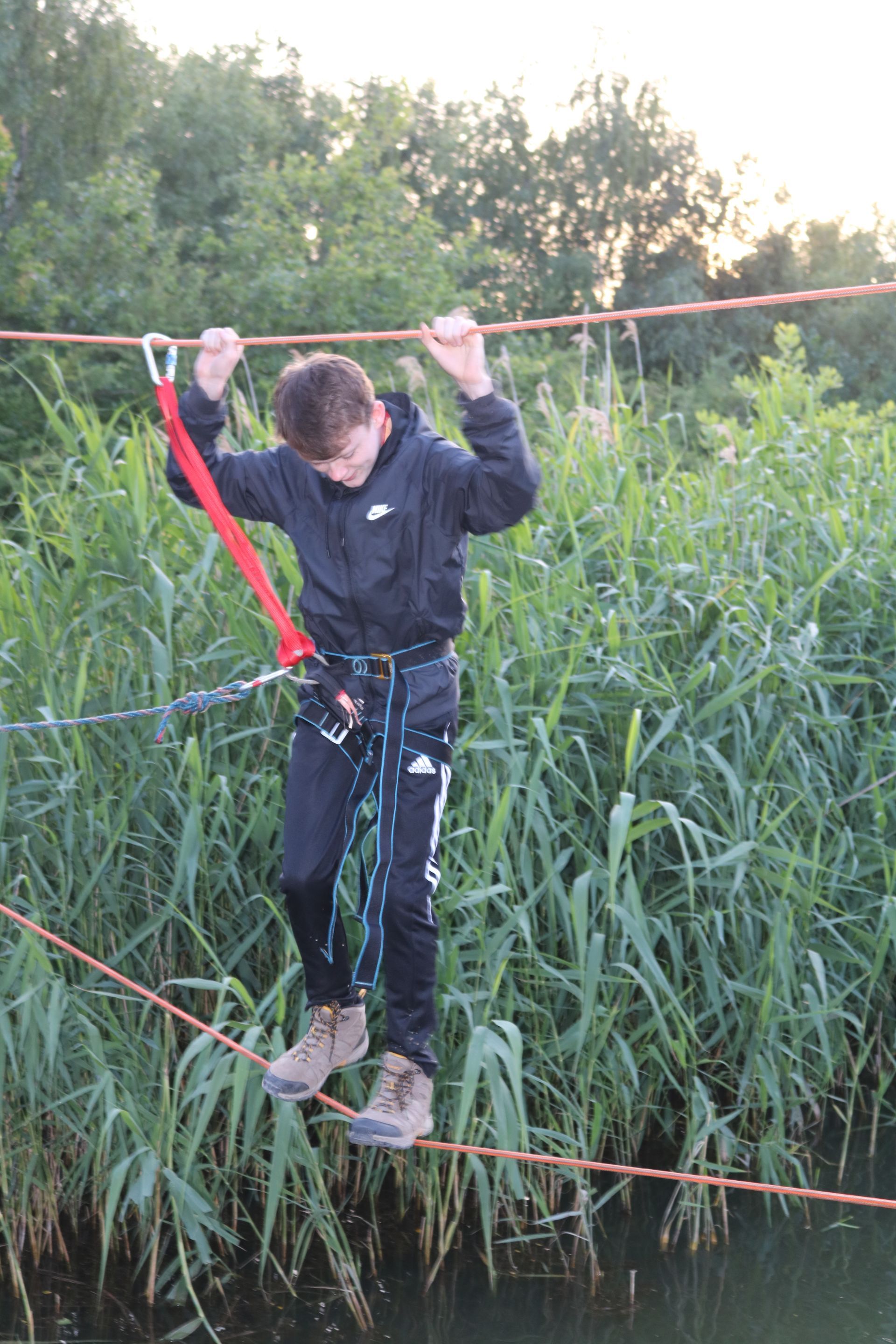 A young man is walking on a rope over a body of water.