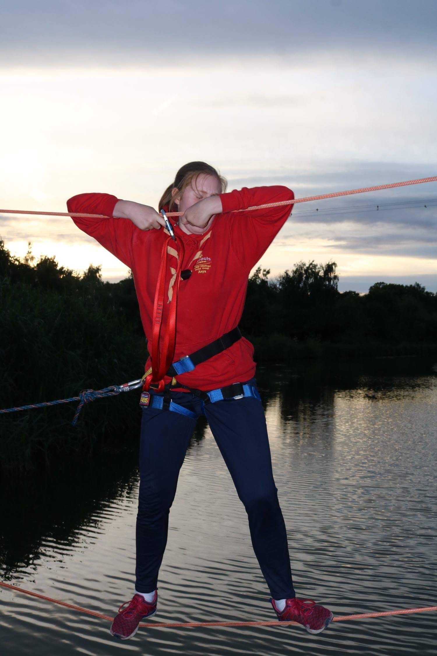 A woman in a red shirt is standing on a rope over a body of water
