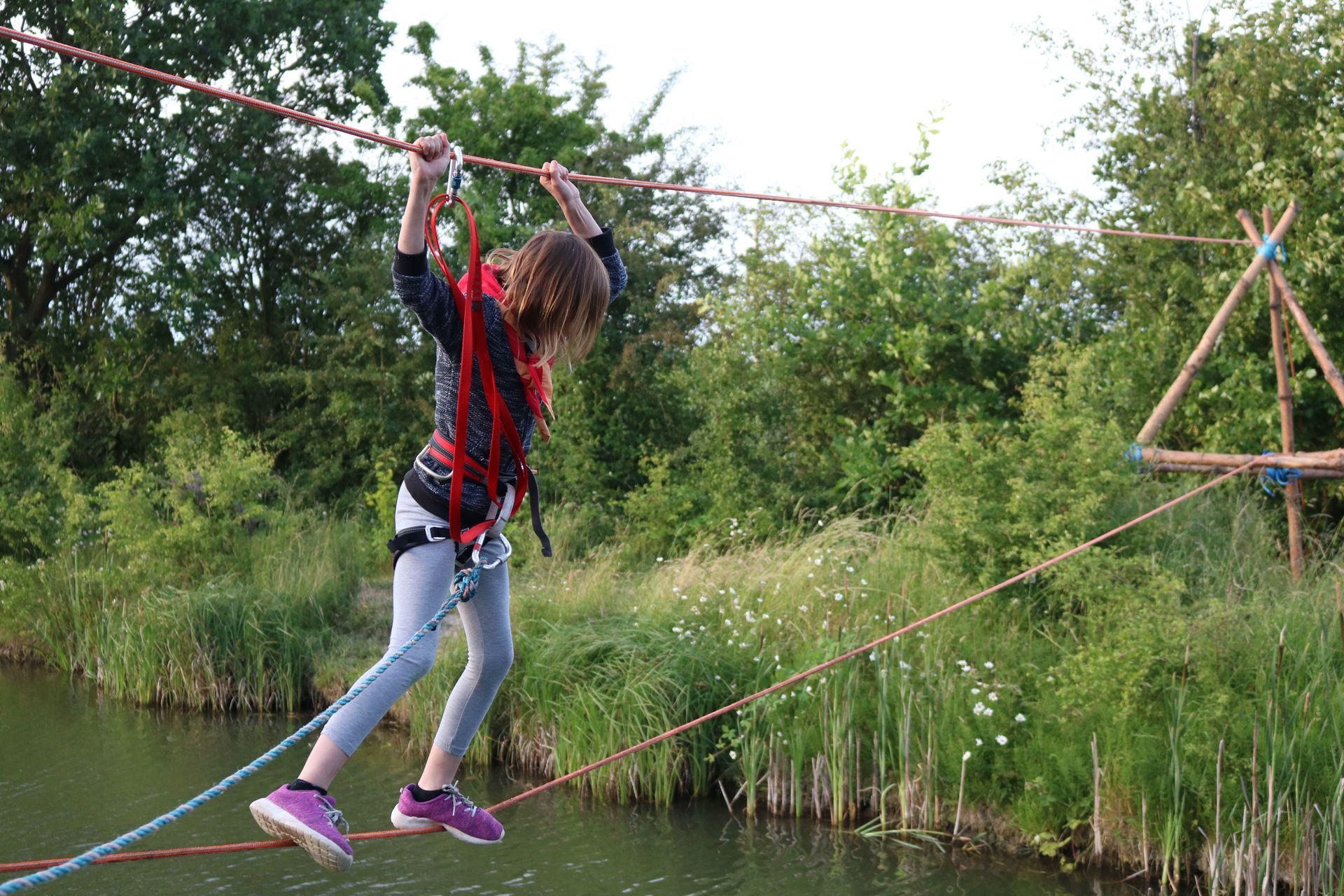 A young girl is walking across a rope bridge over a body of water.