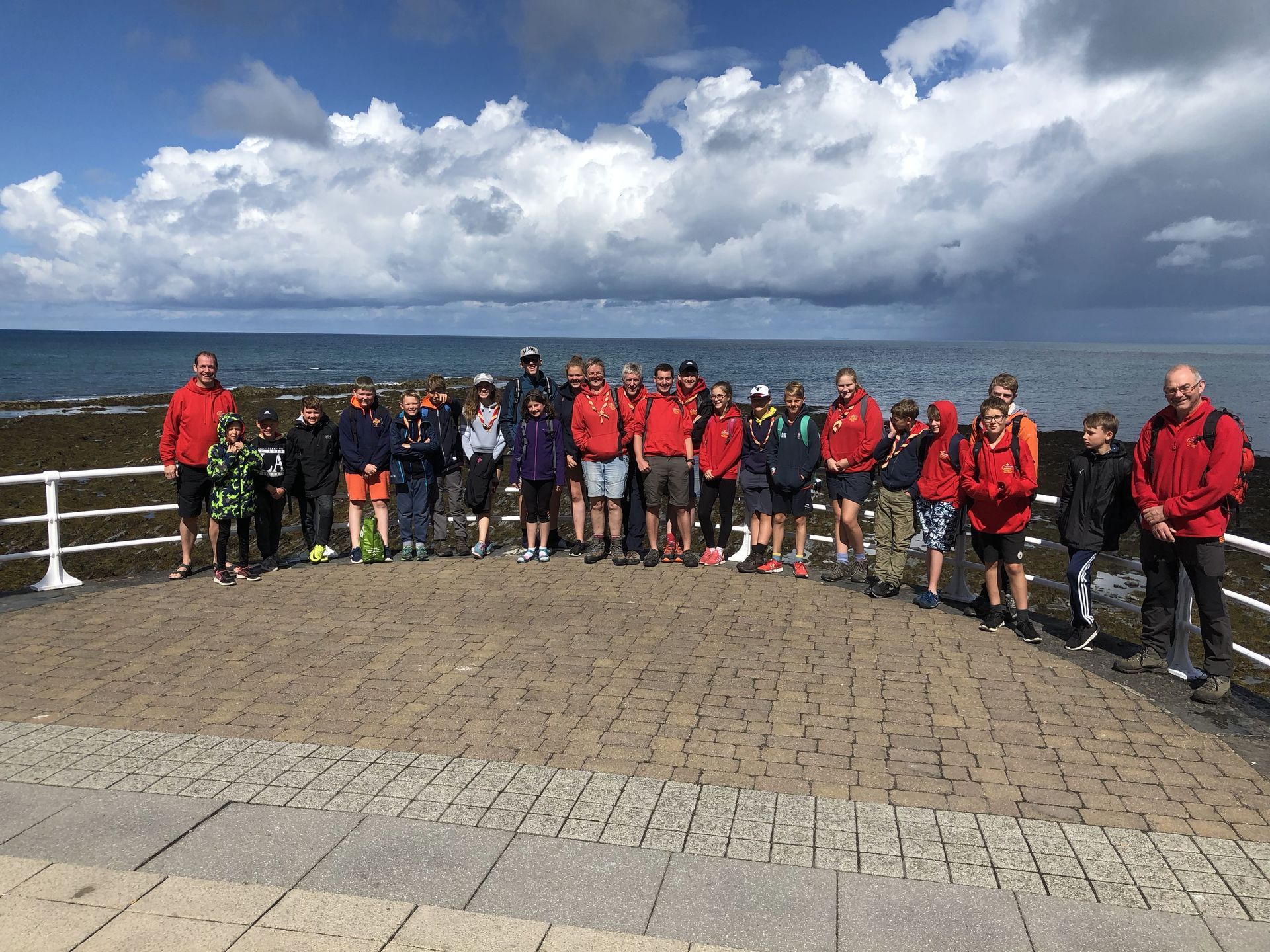 A group of people are standing on a brick walkway next to the ocean.