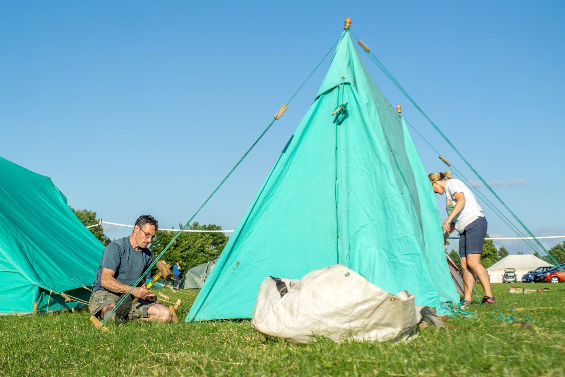 A man and a woman are setting up a tent in a field.