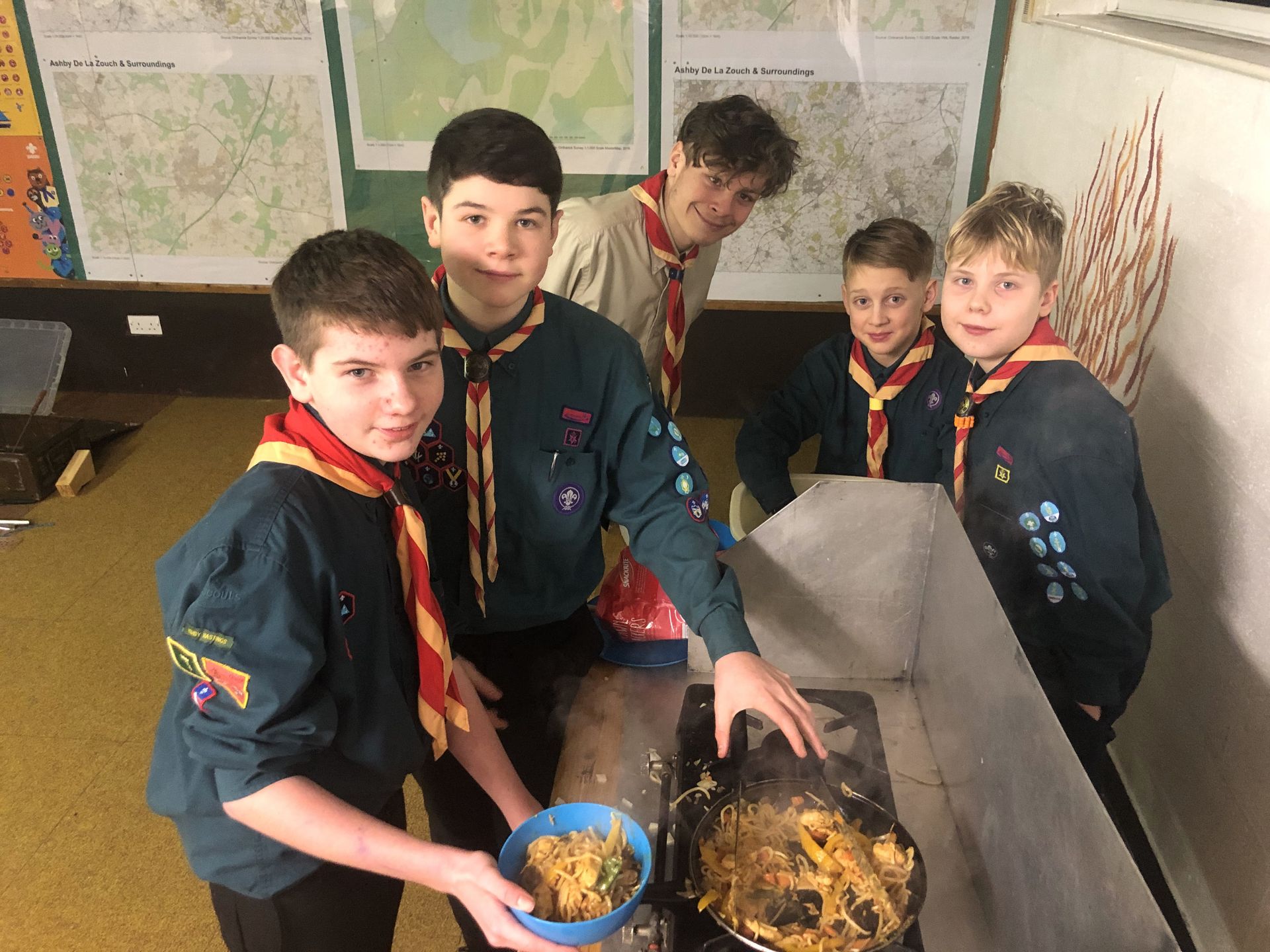 A group of boy scouts are preparing food on a stove.