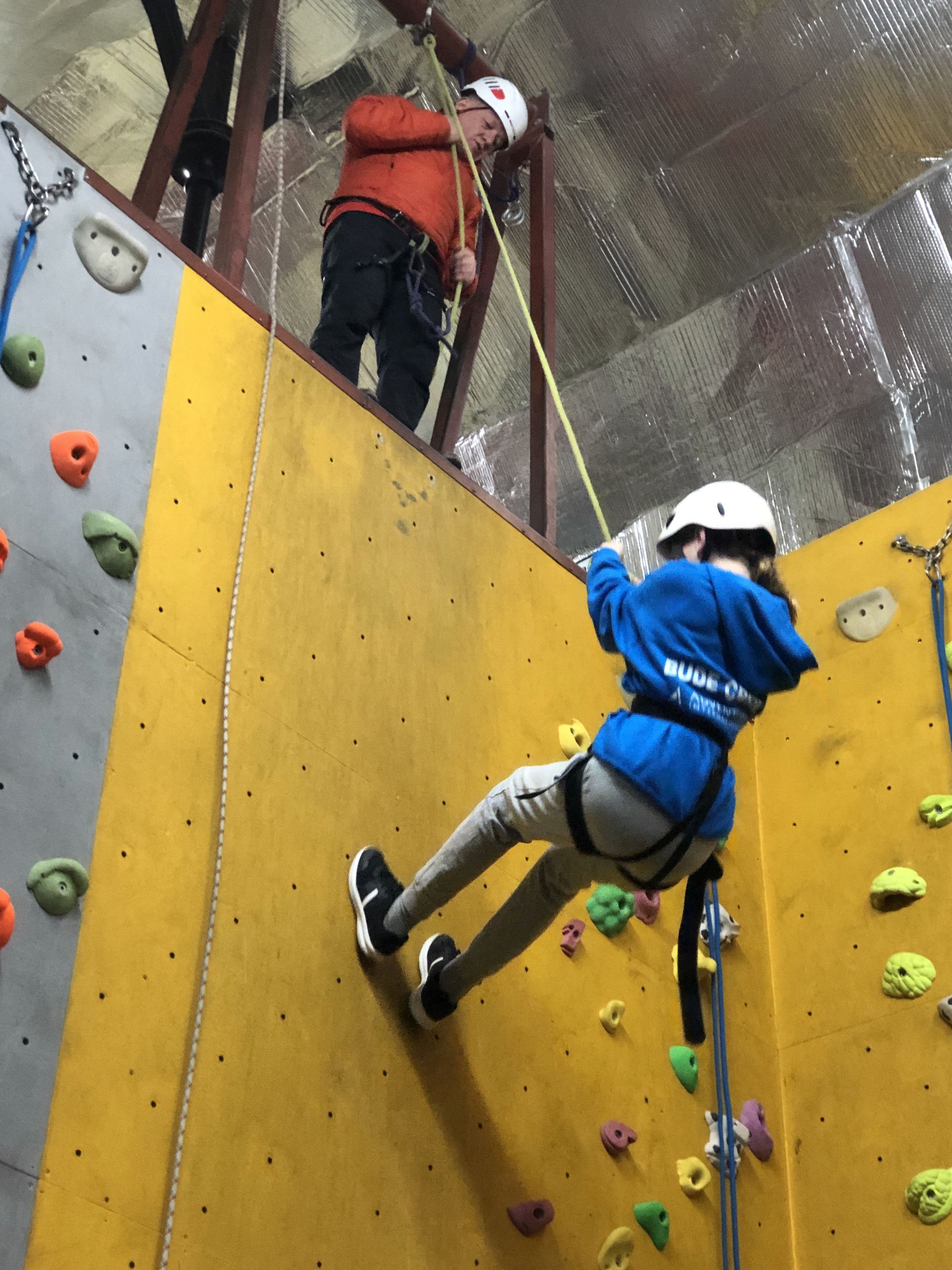 A person in a blue jacket is climbing a climbing wall