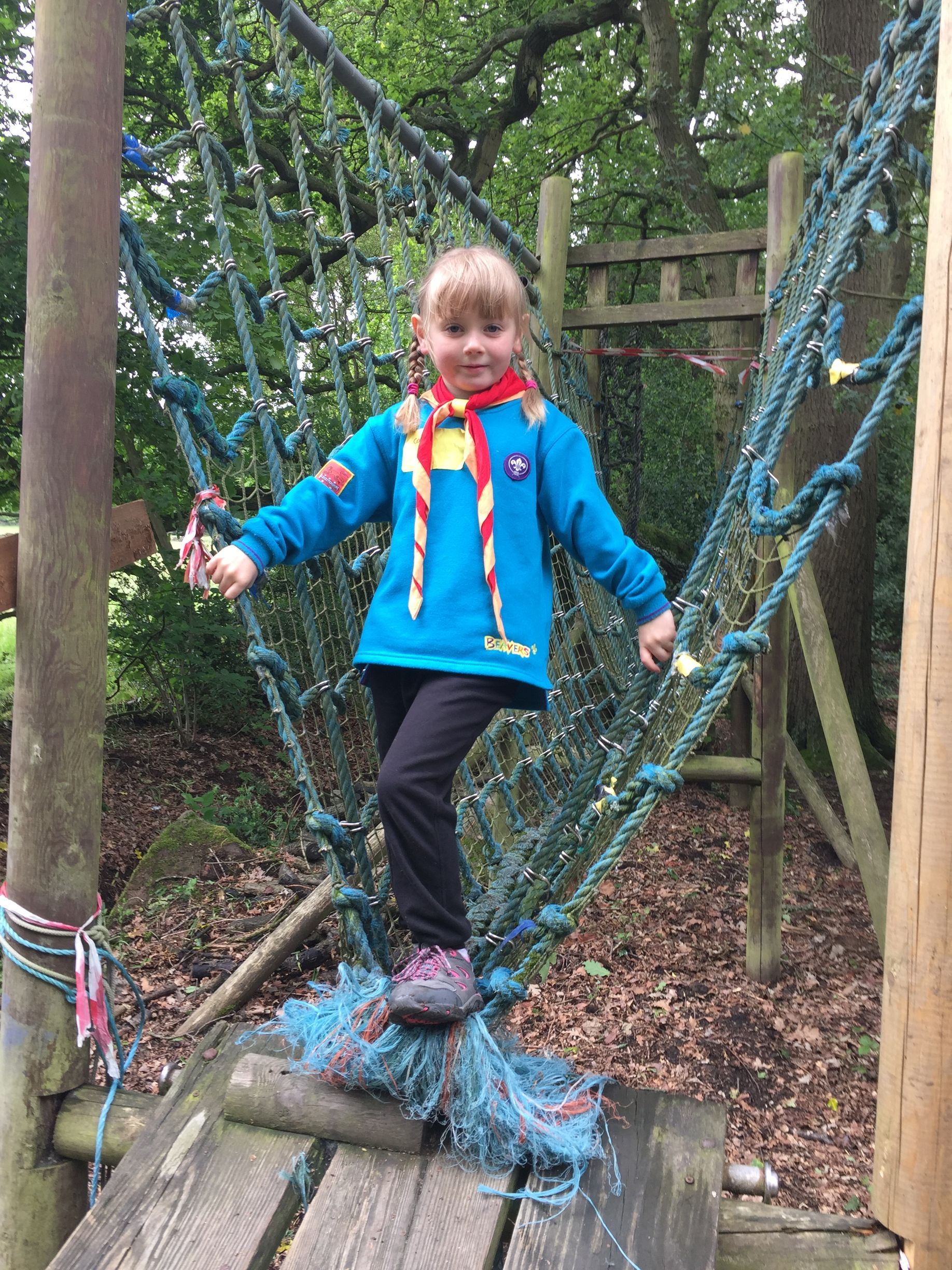 A little girl in a blue jacket is standing on a wooden bridge.