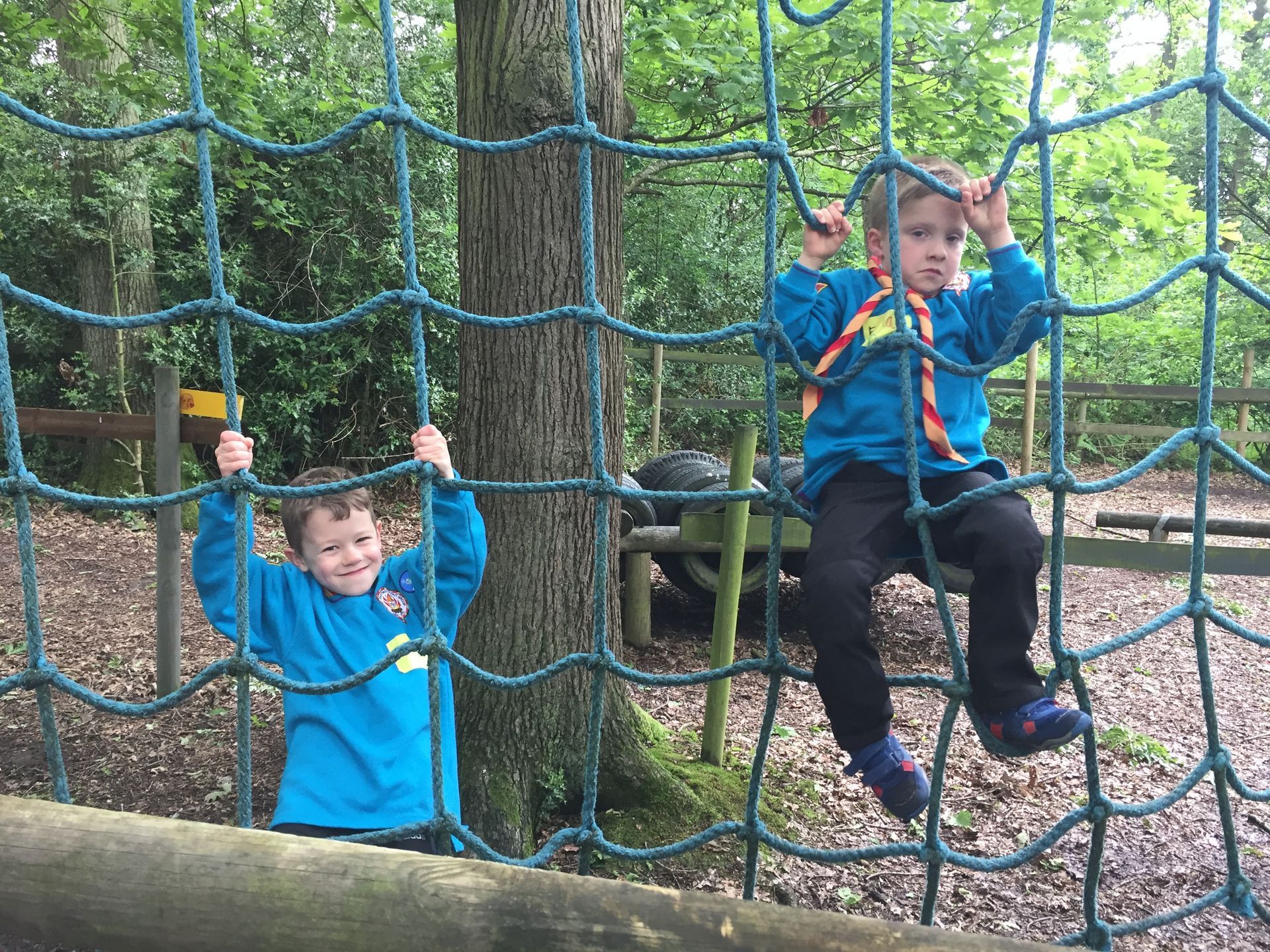 Two young boys are climbing a rope net in the woods.