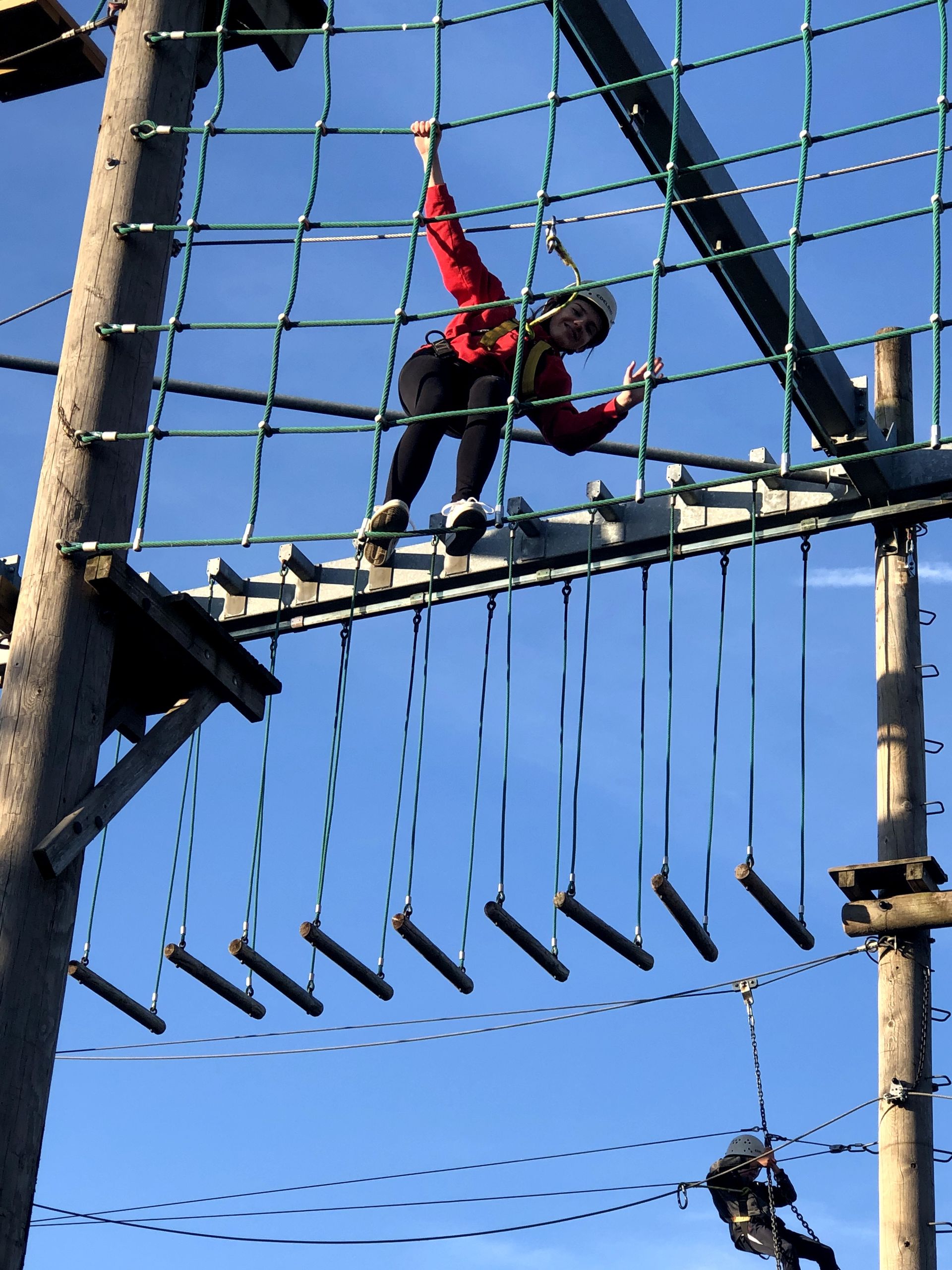 A person is climbing a ropes course with a blue sky in the background