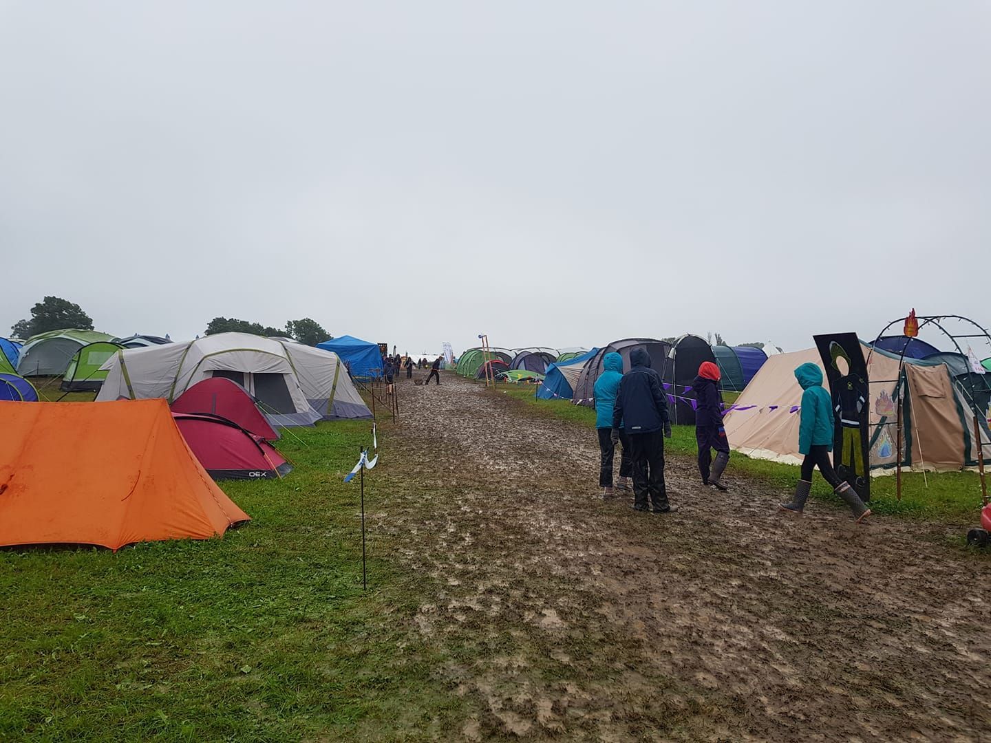A group of people are walking through a muddy field with tents.