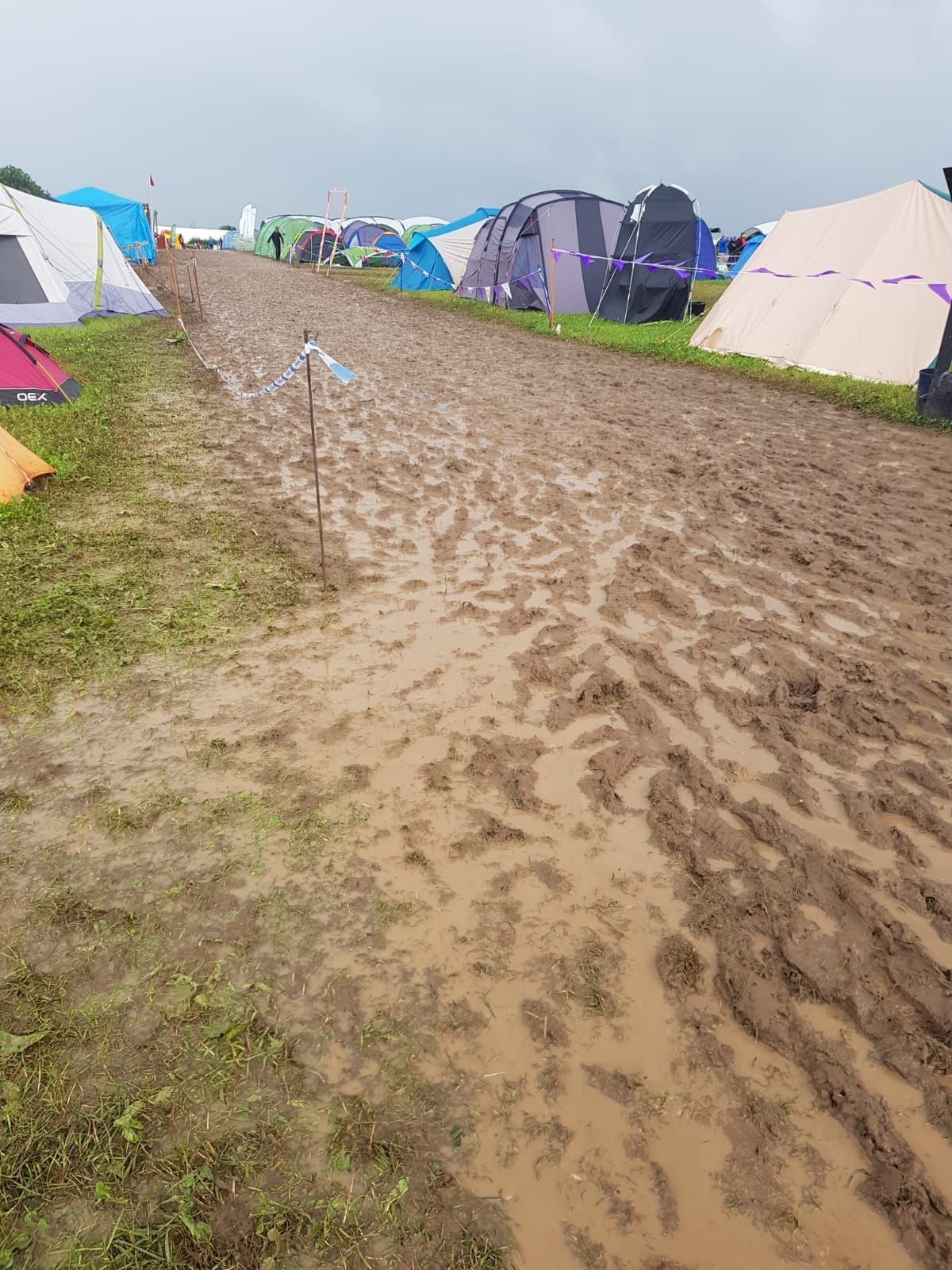 A muddy road leading to a campground filled with tents.