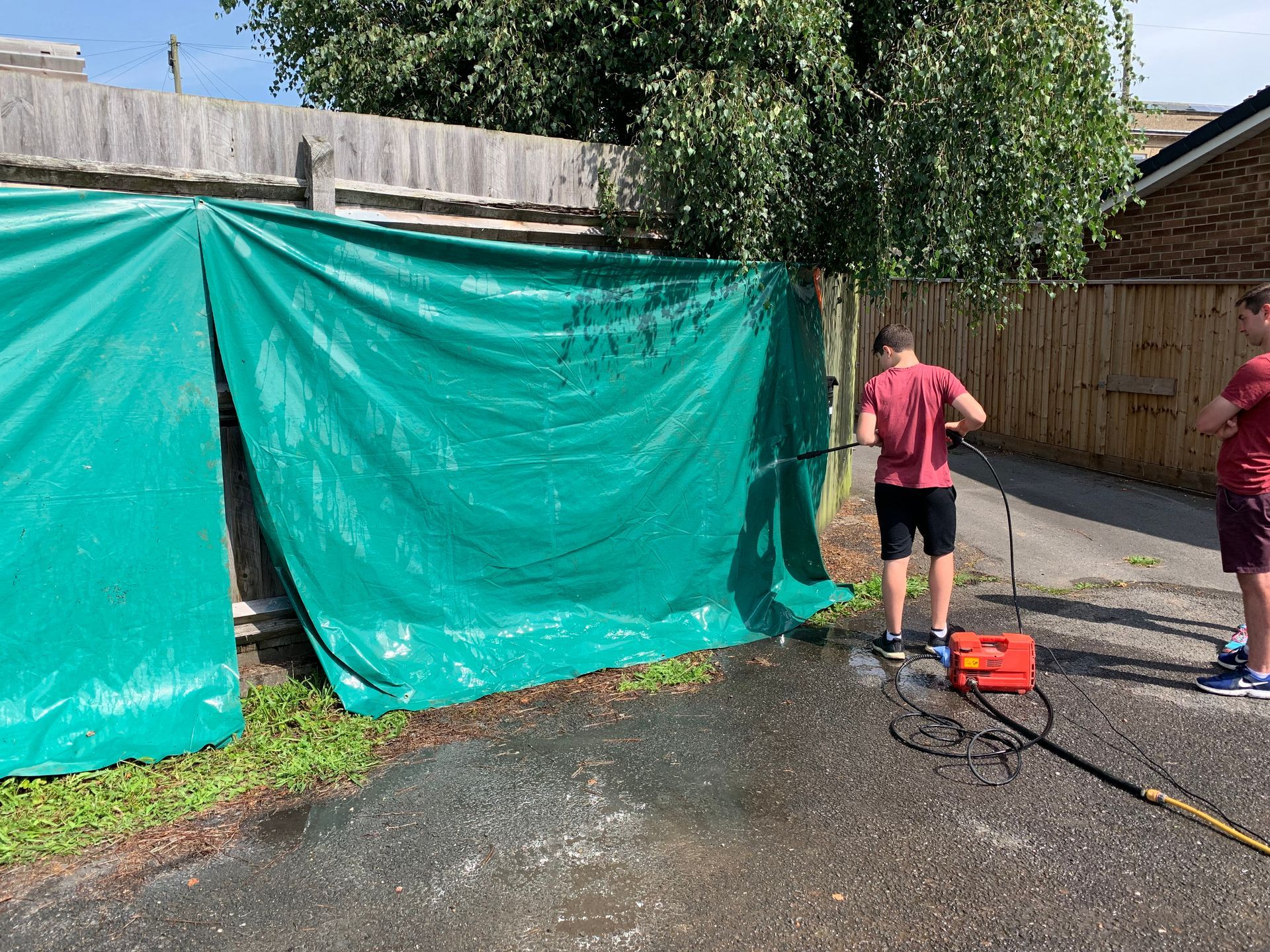 Two people are washing a fence with a high pressure washer.
