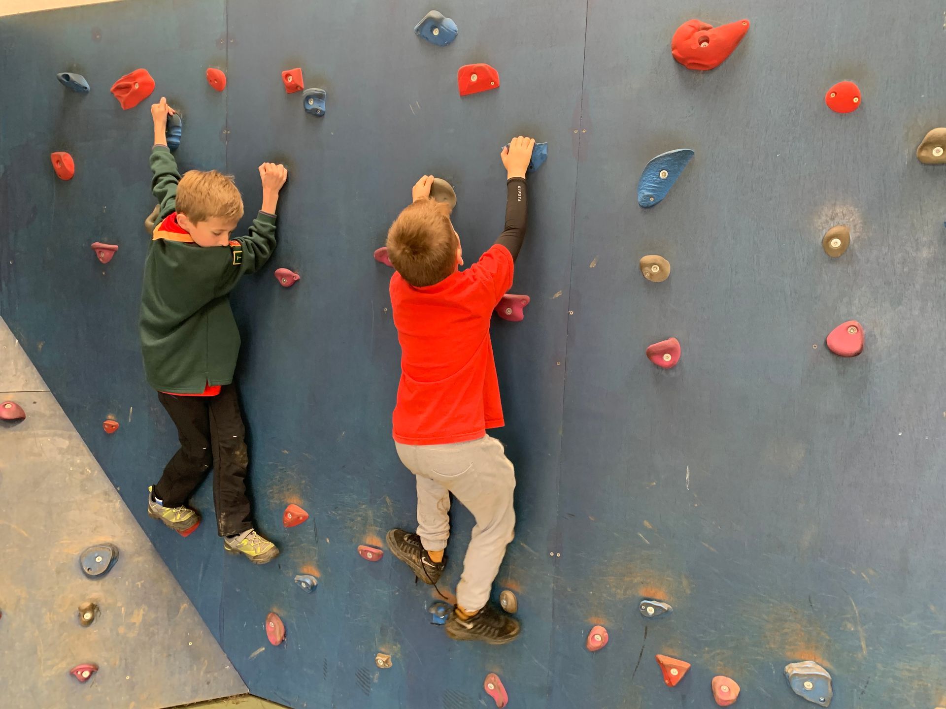 Two young boys are climbing a climbing wall.