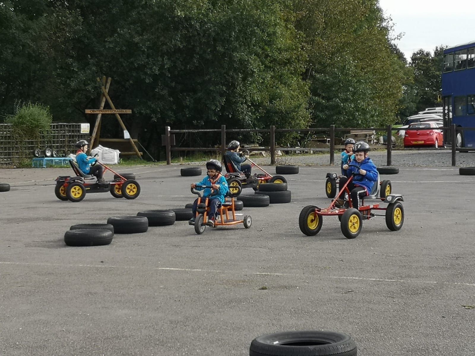 A group of children are riding go karts in a parking lot.