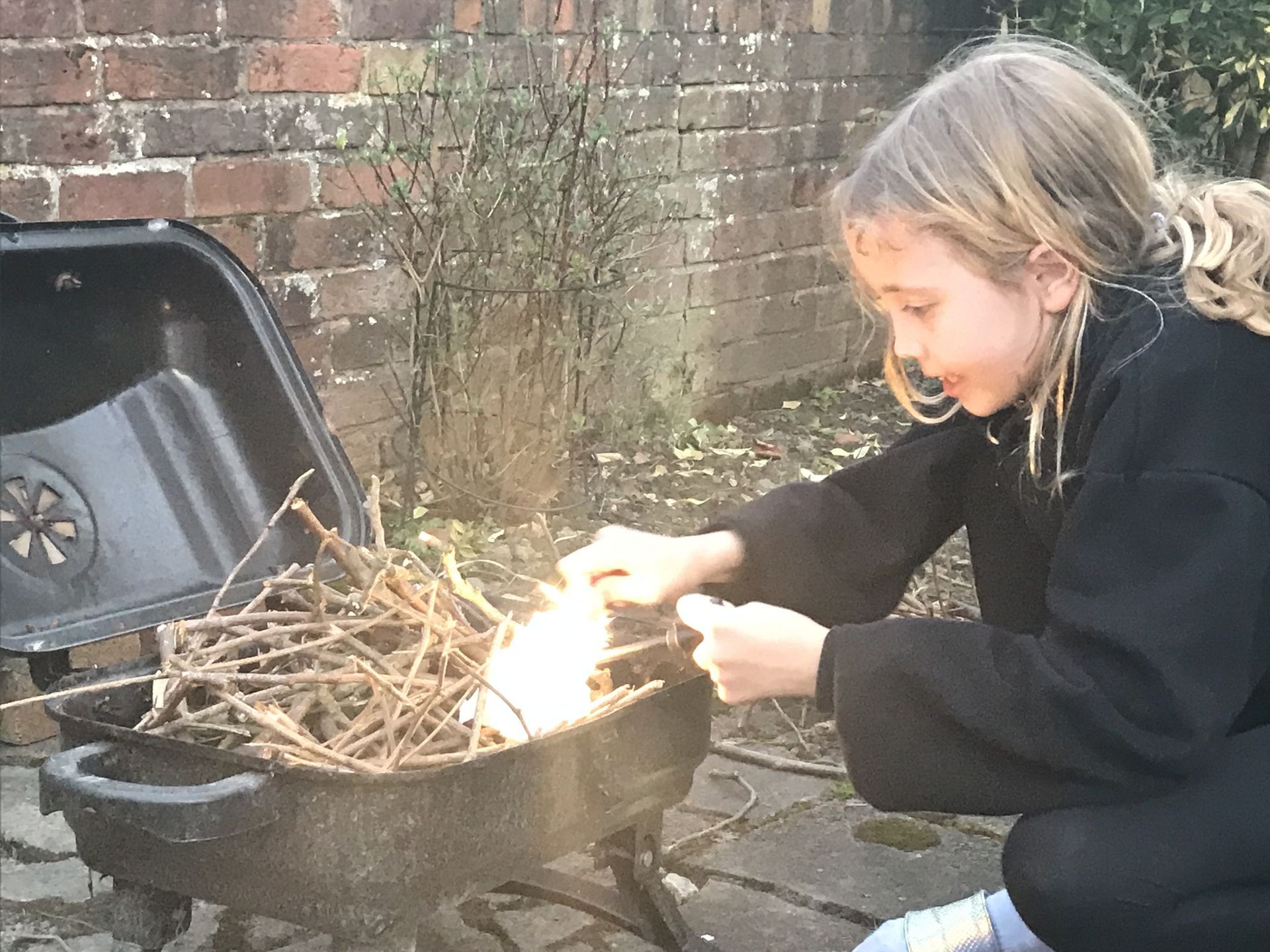 A young girl is lighting a fire in a pot