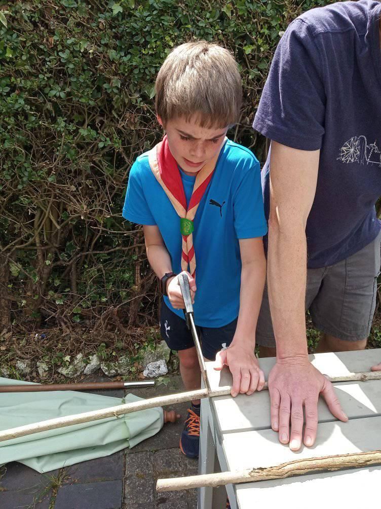 A boy in a blue shirt is cutting a stick with a screwdriver.