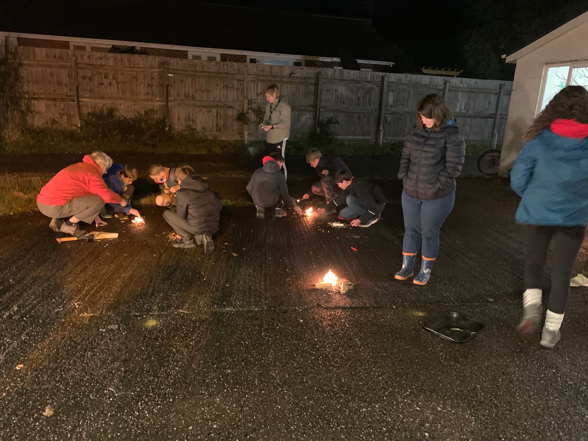 A group of people are lighting candles in a parking lot at night.