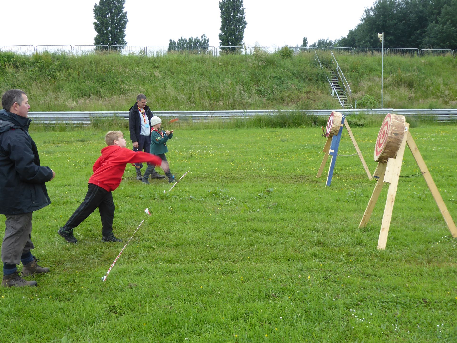 A boy in a red jacket is throwing an arrow at a target