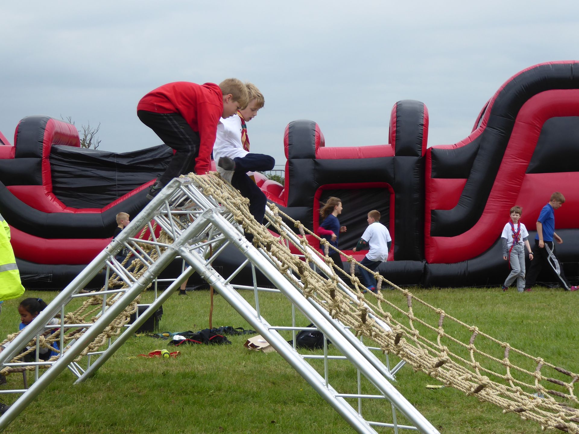 A group of children are playing on a ropes course in front of an inflatable obstacle course.