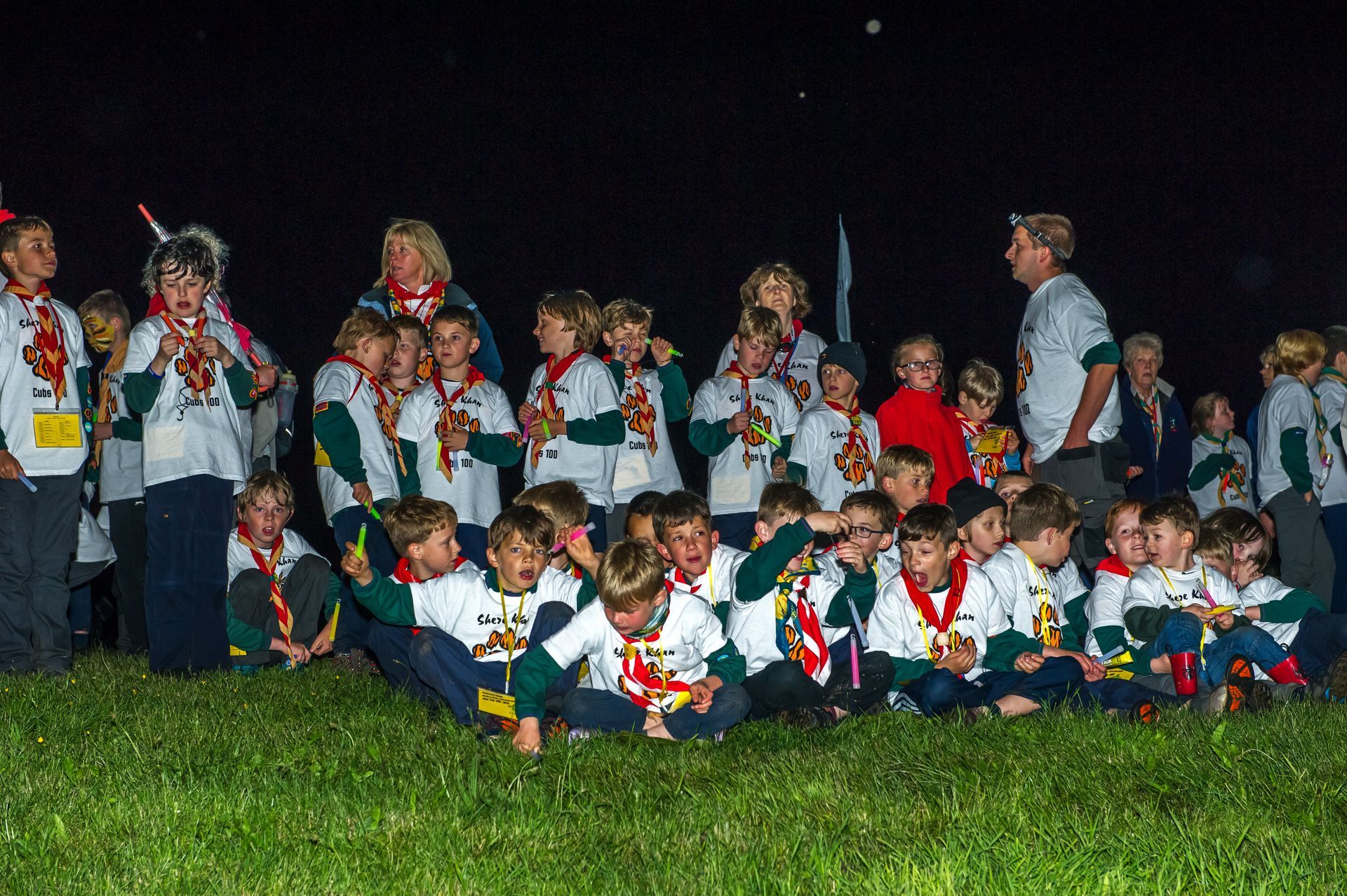 A group of children are sitting in the grass at night.