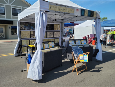 Tent display at an outdoor market with framed items, books, and signage; people are browsing.