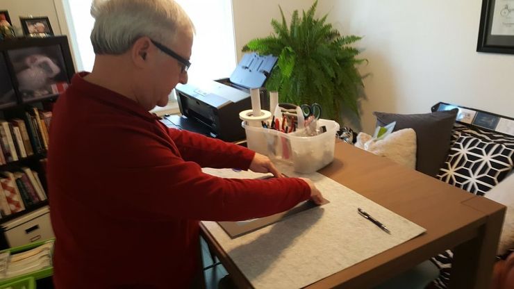 Person in a red sweater writing on a notepad at a table in a home dining room.