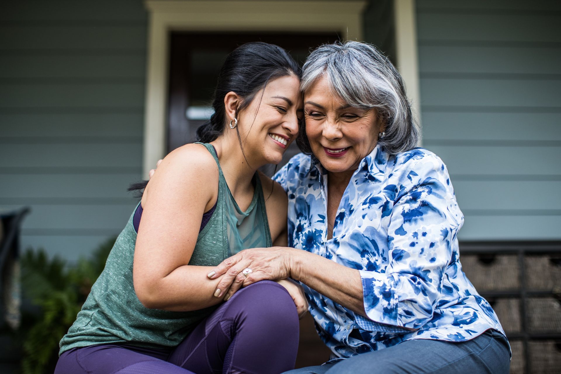 Two women are sitting on the porch of a house and hugging each other.