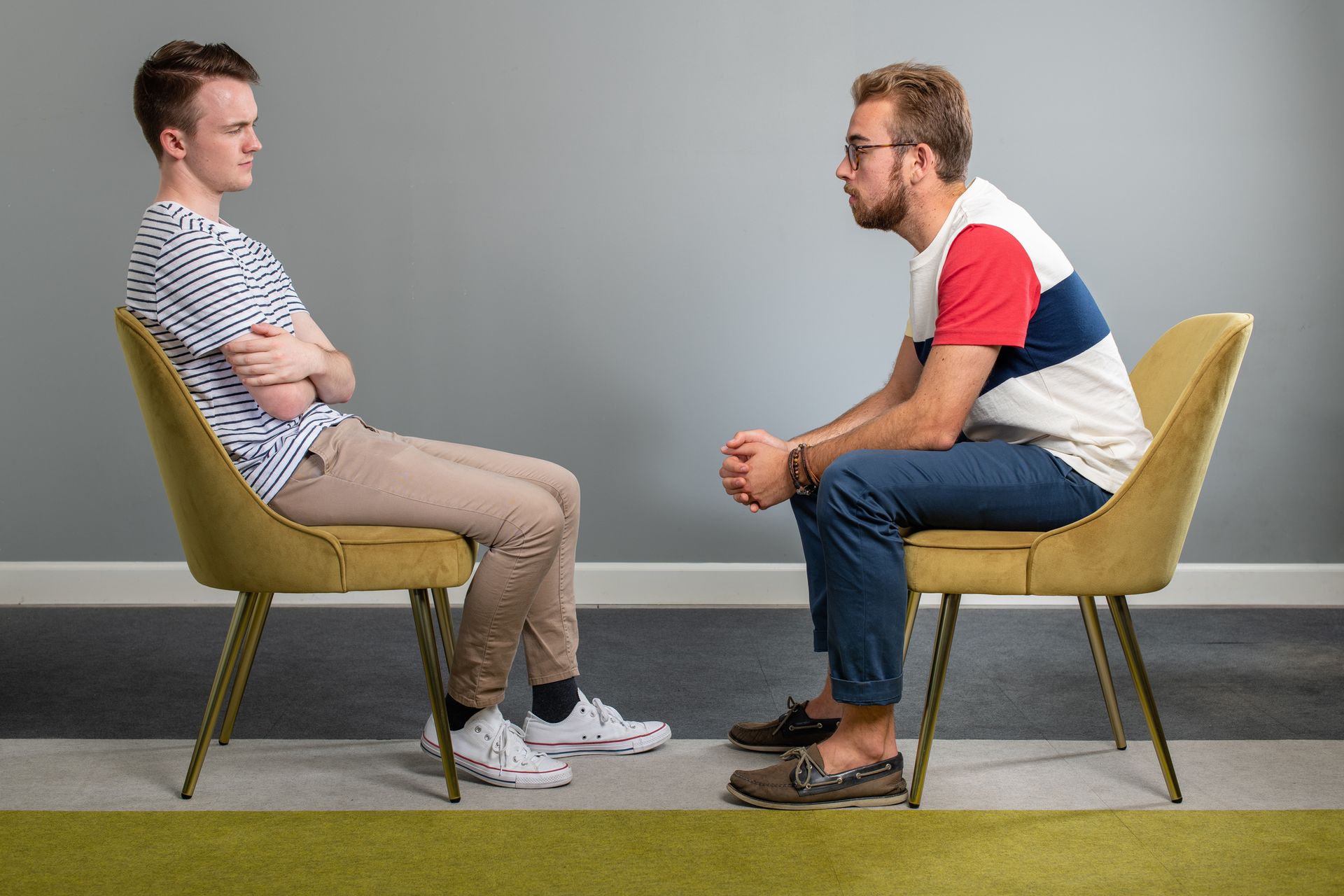 Two men are sitting in chairs talking to each other.