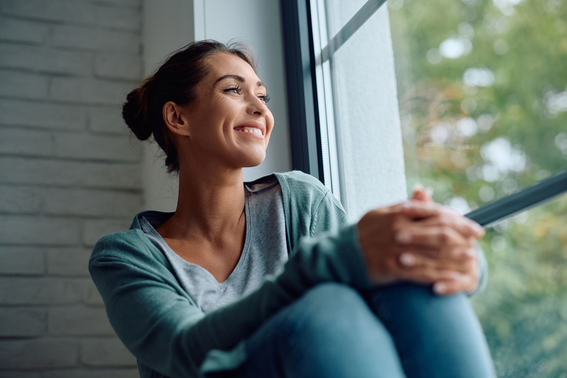 A woman is sitting on a window sill looking out the window. A woman is sitting on a window sill looking out the window.