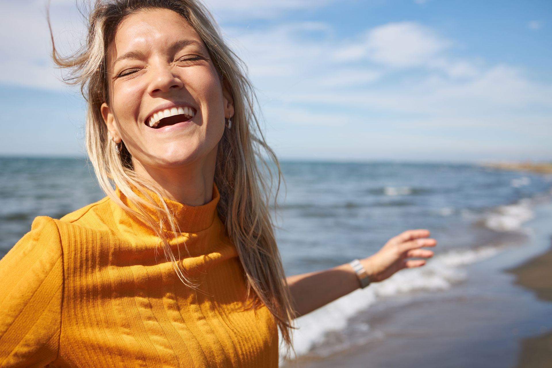 A woman in a yellow shirt is laughing on the beach.