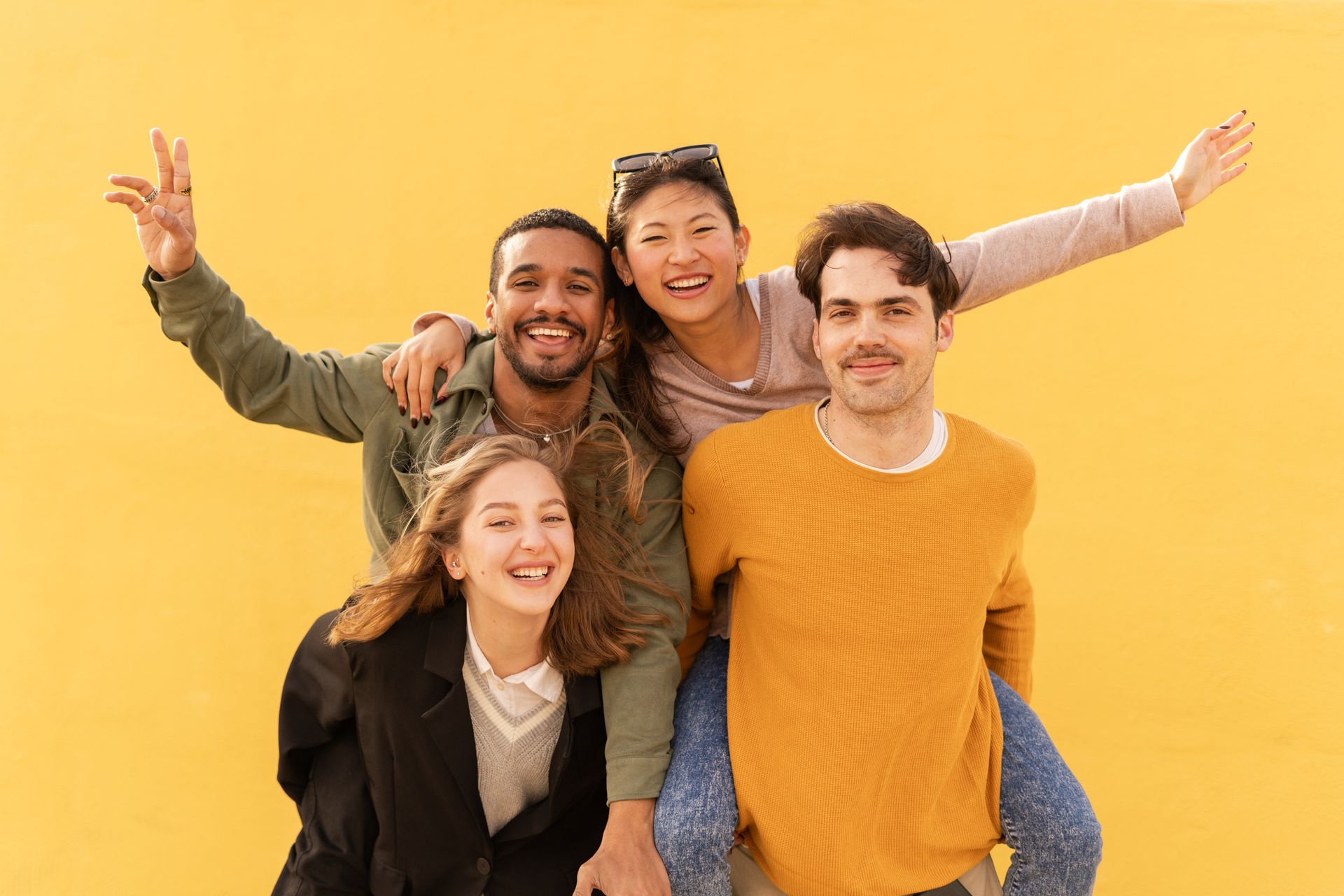 A group of young people are posing for a picture in front of a yellow wall.