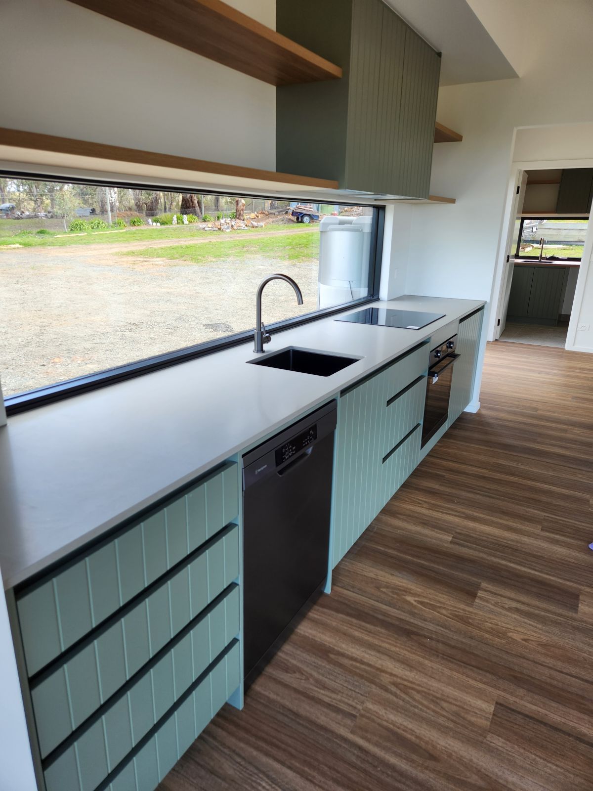 Modern kitchen with sage green cabinets, light countertop, stainless steel appliances, and large window.