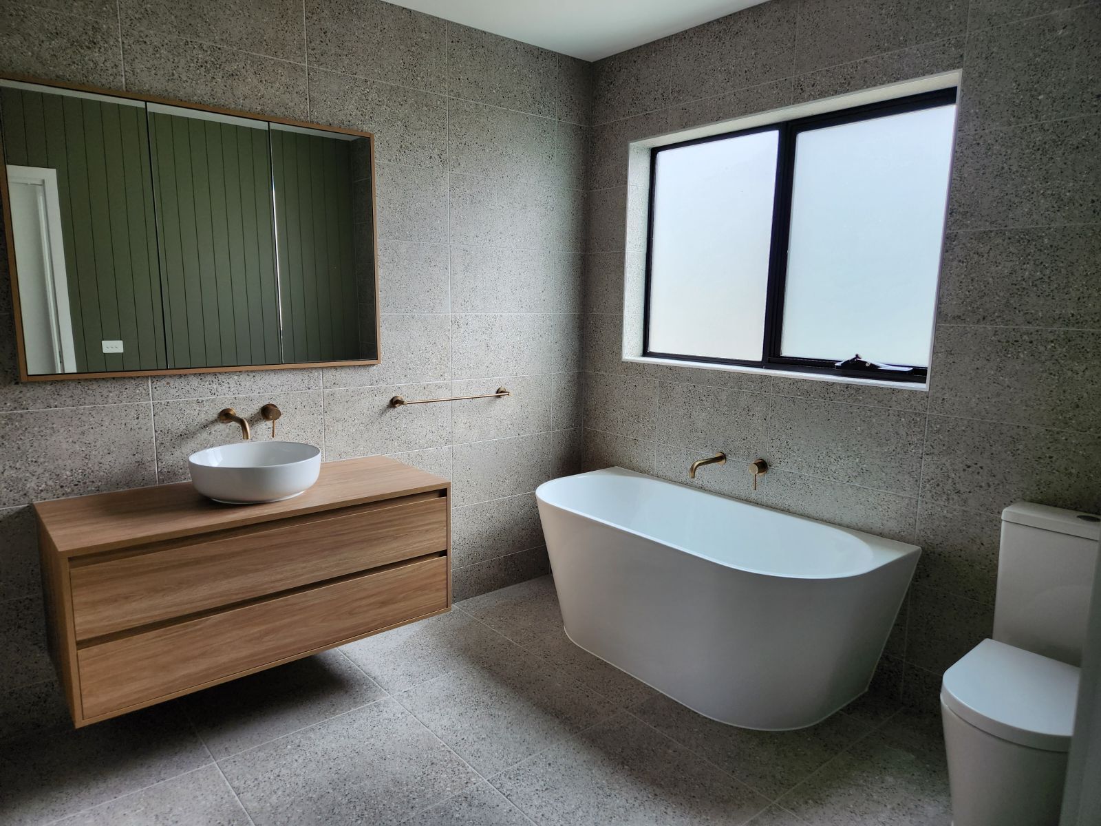 Modern bathroom with a freestanding tub, wood vanity, and terrazzo walls.