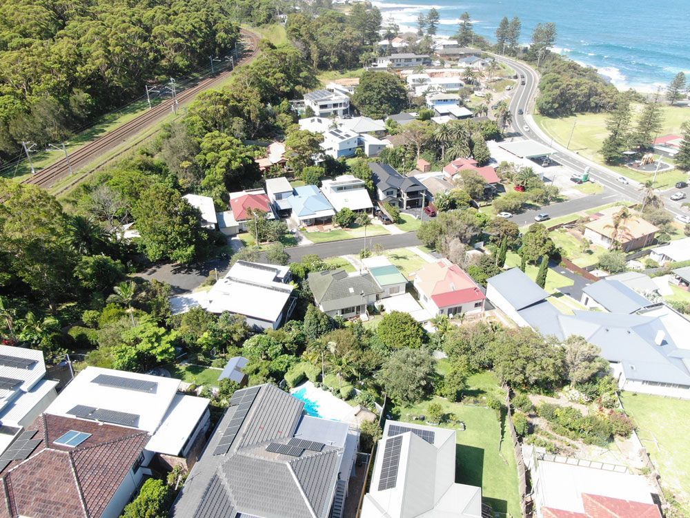 Aerial view of coastal town with houses, a road, railroad tracks, and trees.
