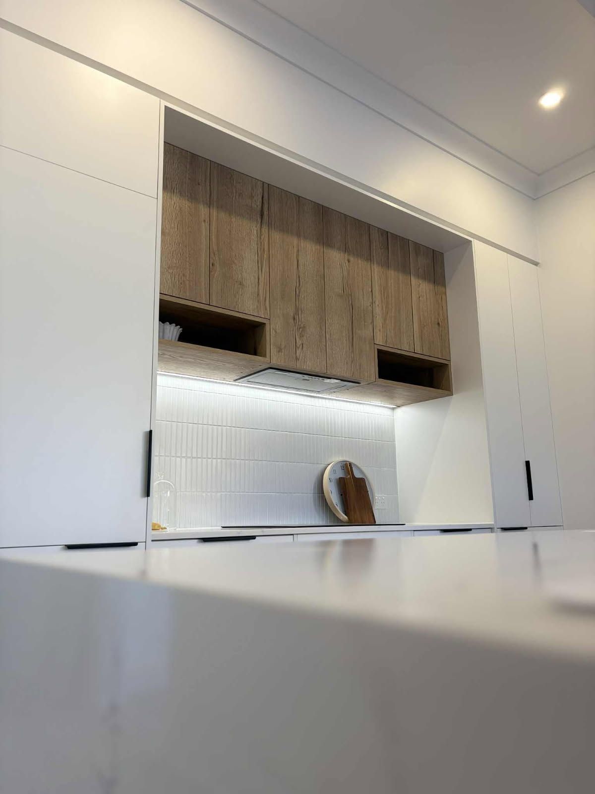 Kitchen with white cabinetry and wooden upper cabinets, white backsplash, and a white countertop.