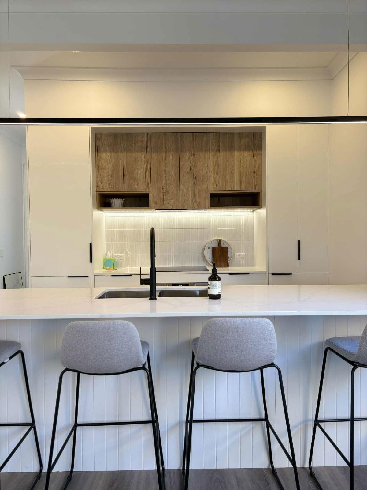 Modern kitchen with white cabinets, wood accents, black faucet, and bar stools.
