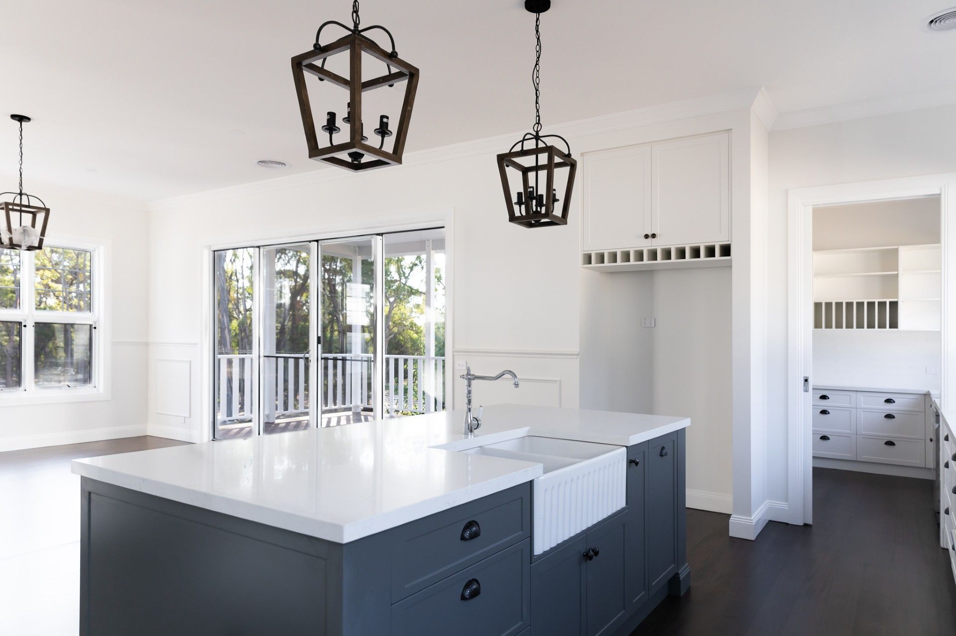 Kitchen with gray island, white countertops, and dark pendant lights, leading to a balcony.