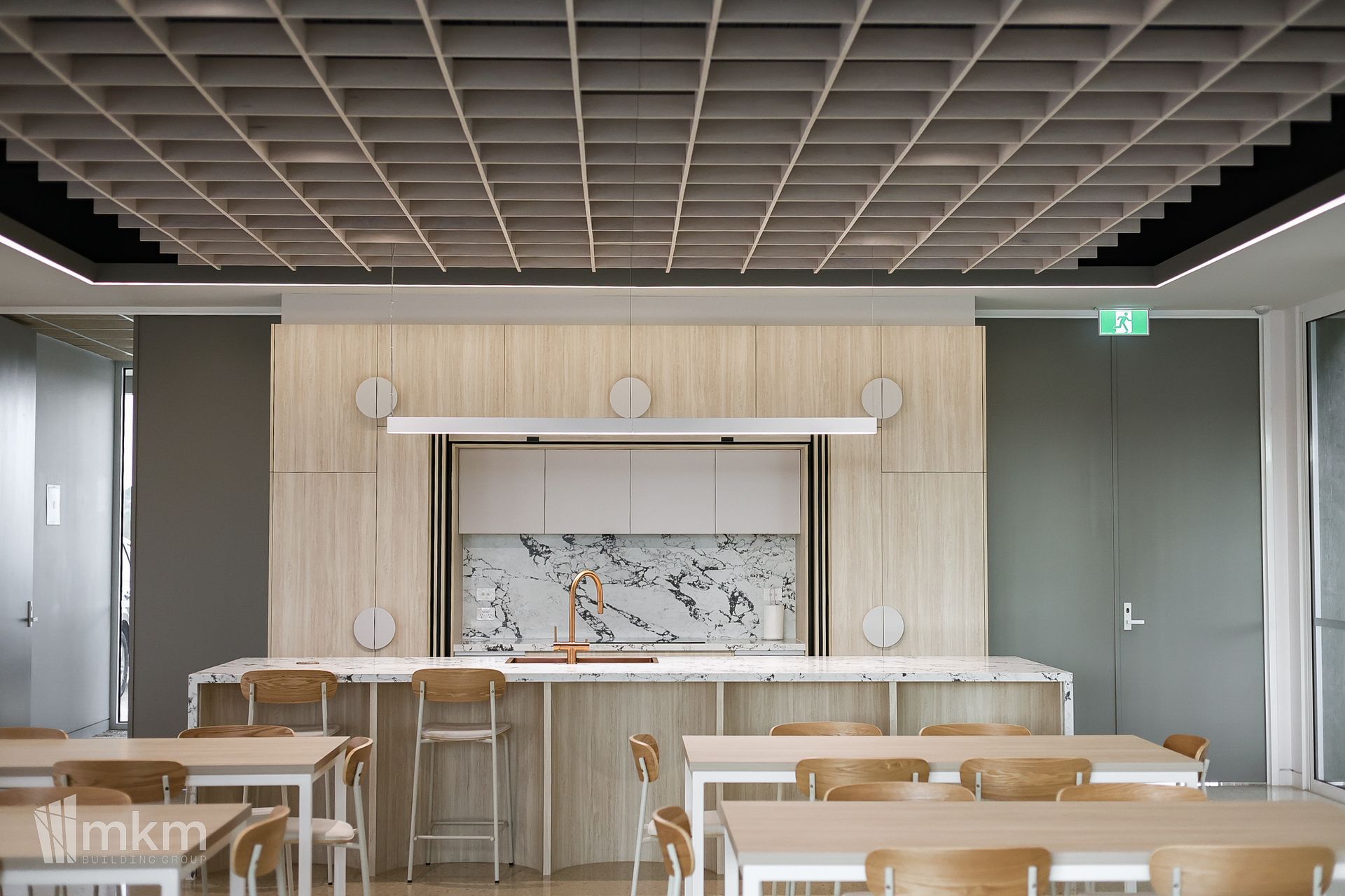 Modern interior with a kitchen island and tables. Grid ceiling, marble backsplash, and wooden chairs.