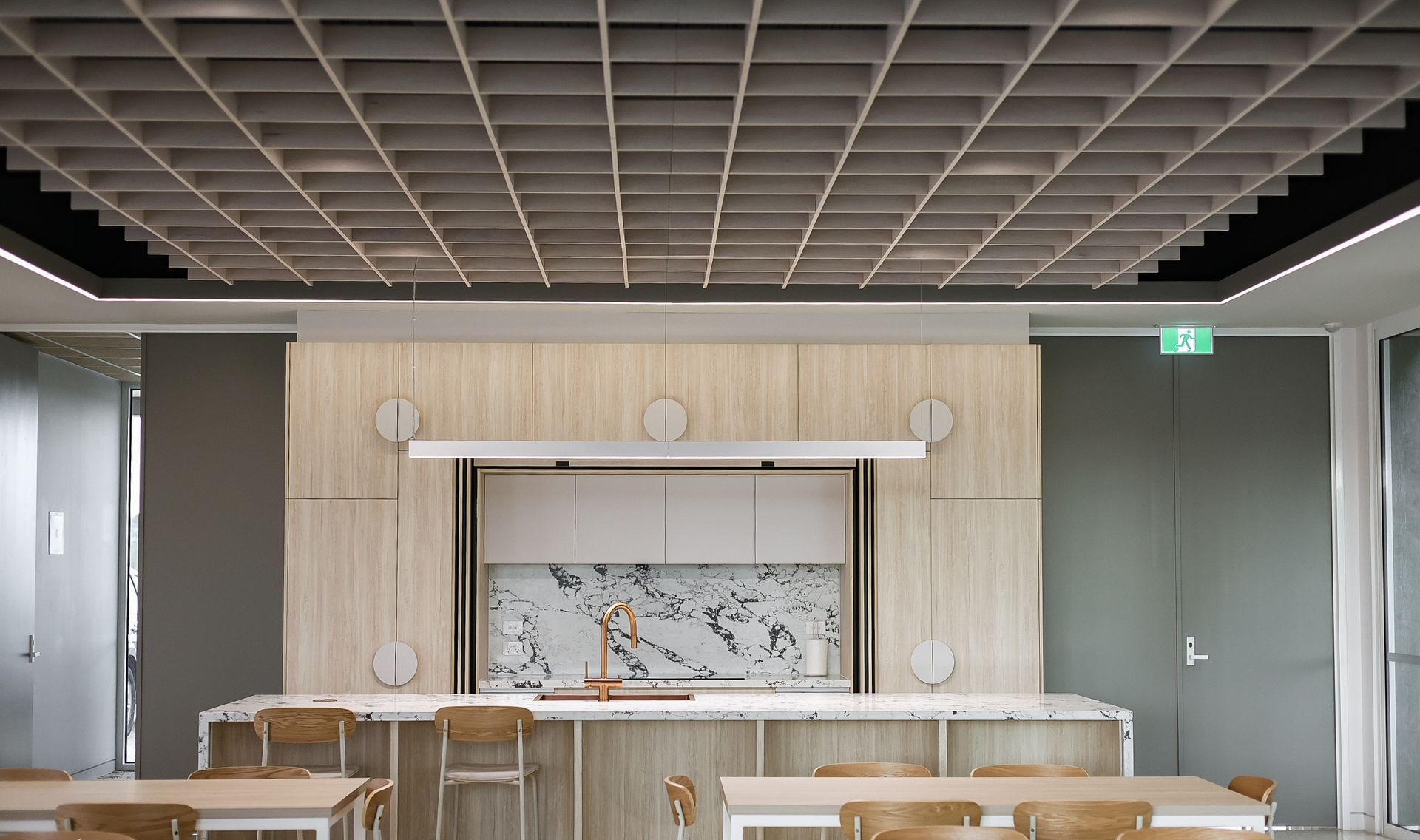 A modern kitchen area with wood cabinets, marble backsplash, grid ceiling, and chairs at a counter.