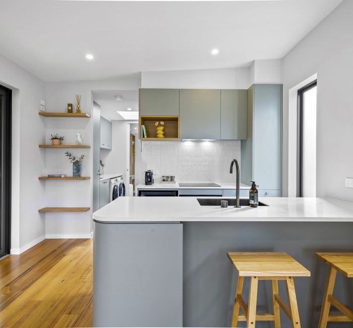 Modern kitchen with gray cabinetry, white countertops, wooden stools, and hardwood floors.
