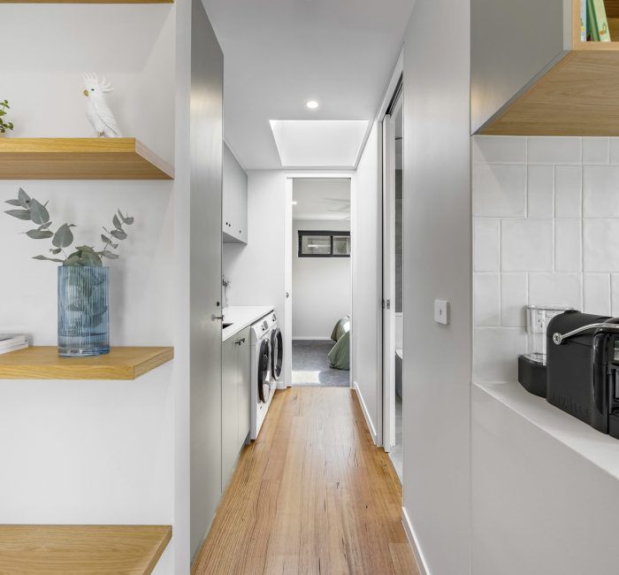 Narrow hallway with washing machine, shelves, and wood floors.