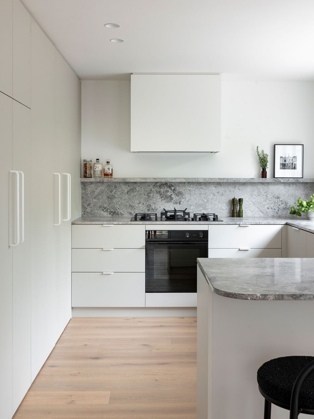 Modern white kitchen with light wood floors and gray stone countertops.