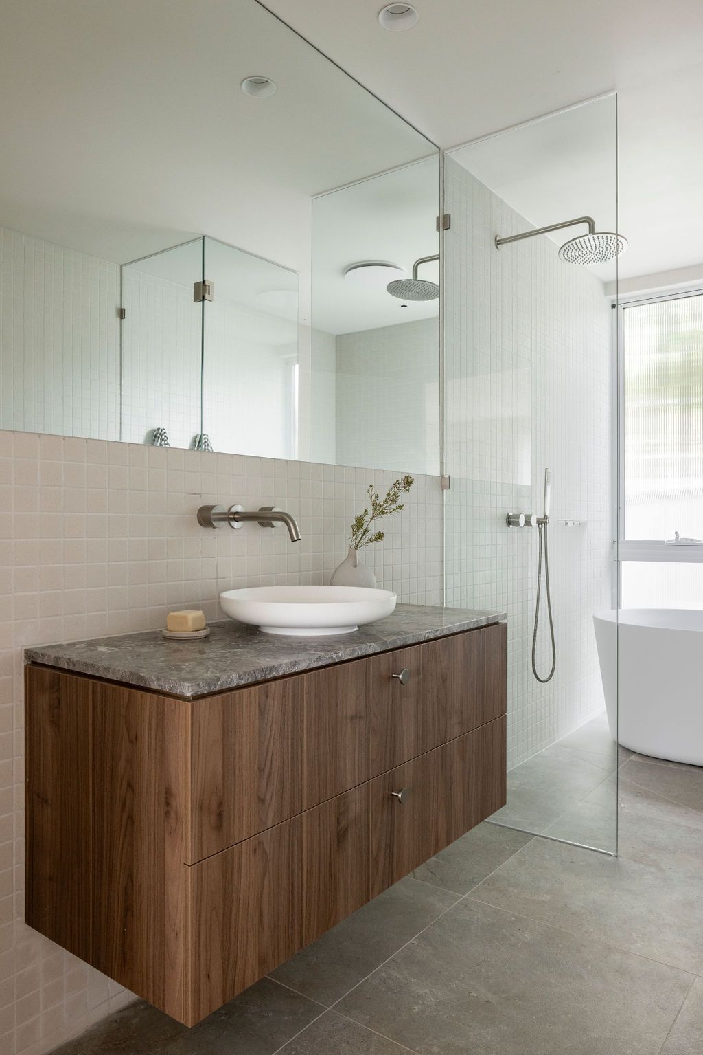 Modern bathroom with floating wooden vanity, white vessel sink, and glass shower enclosure.