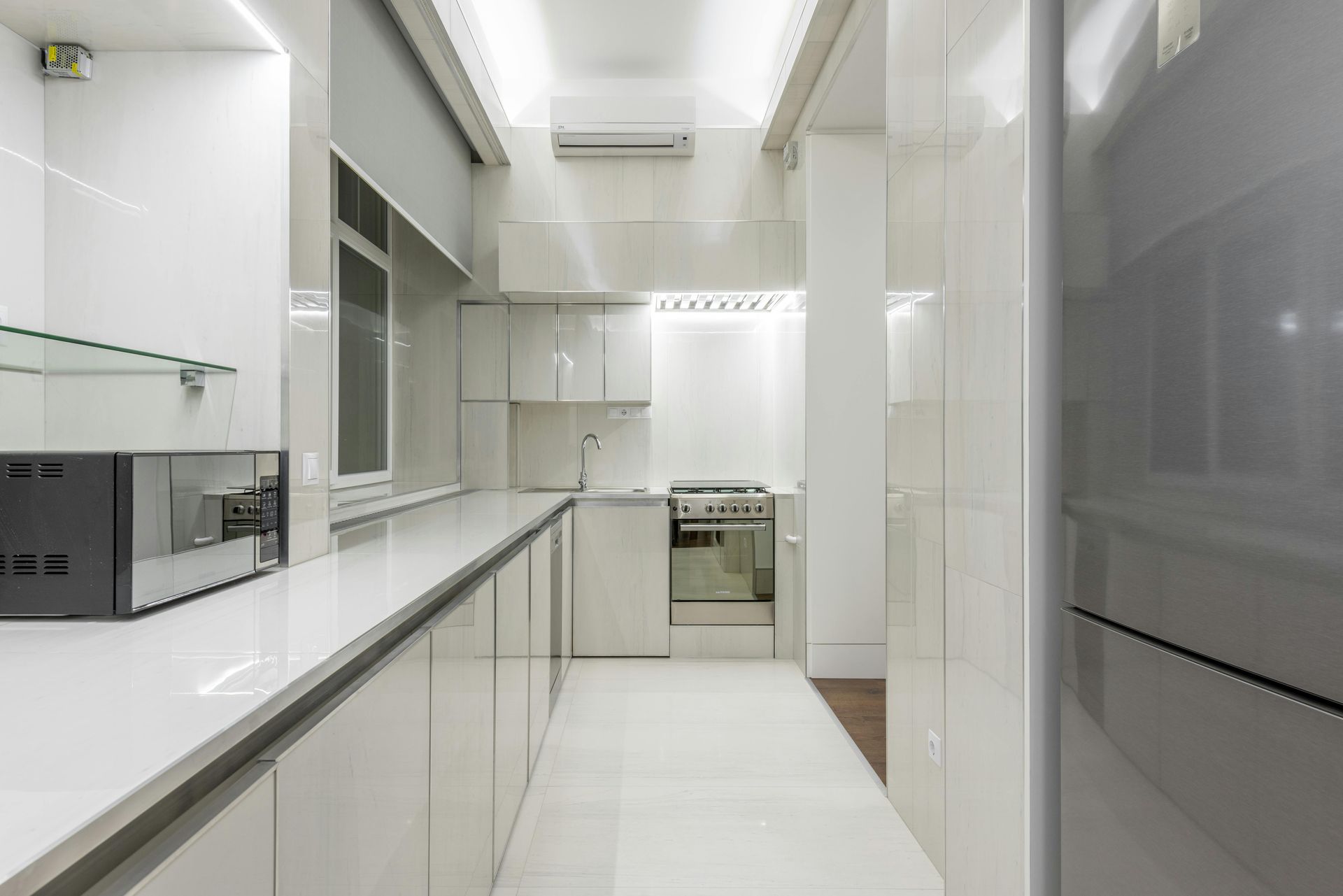 White modern kitchen with glossy cabinets, stainless steel appliances, and tile floor.