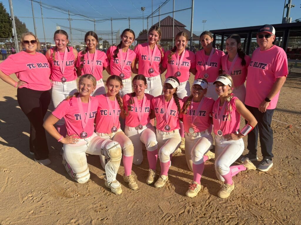 Softball team in bright pink jerseys posing on a field after a game