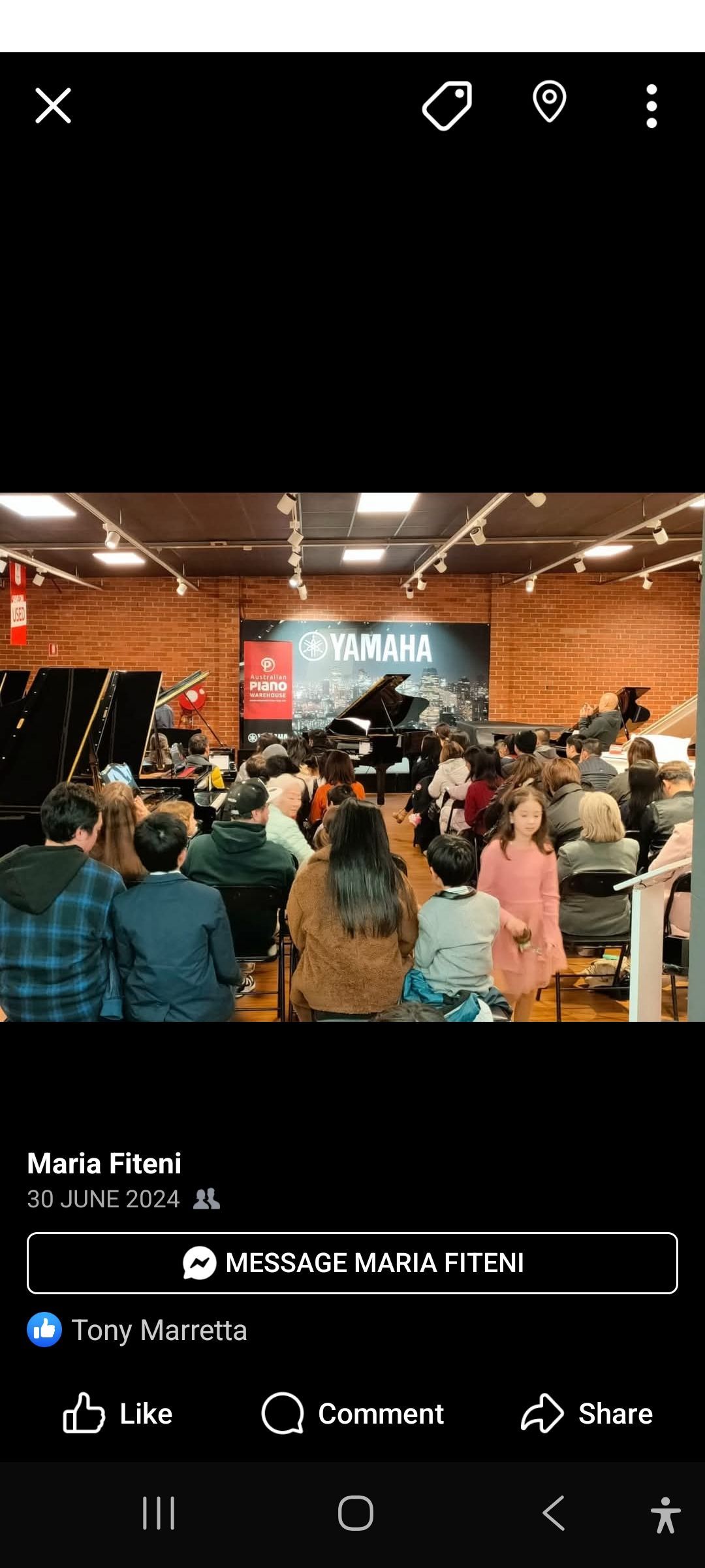 A crowd gathered indoors watching a performance with a large sign in the background that says