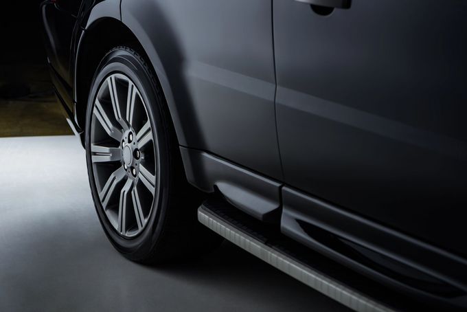 Primo piano della ruota posteriore e del predellino laterale di un SUV nero in un garage poco illuminato.