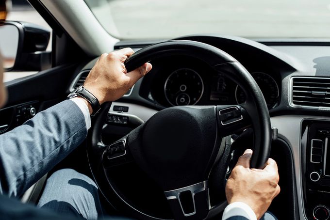 Mani sul volante all'interno di un'auto, mentre si guida su strada.