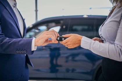Due persone si scambiano le chiavi dell'auto accanto a un'auto blu scuro.