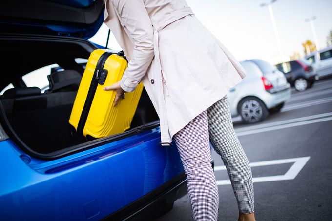 Una persona carica una valigia gialla nel bagagliaio di un'auto blu in un parcheggio.