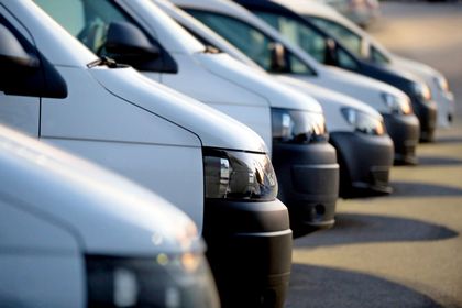 Una fila di furgoni e auto parcheggiati ad angolo lungo una strada illuminata dal sole.