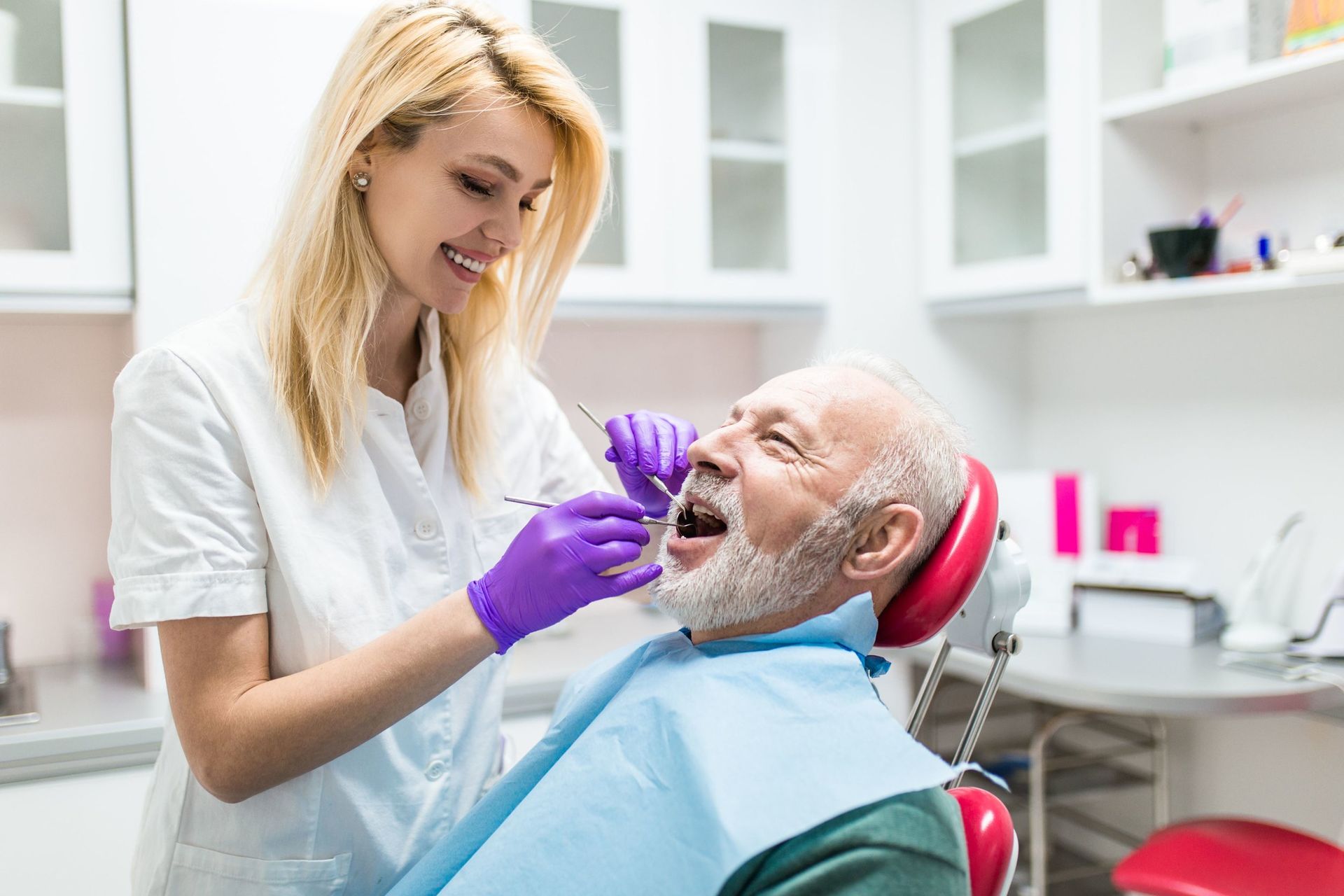 a woman is examining a senior citizen man 's teeth in a dental office .