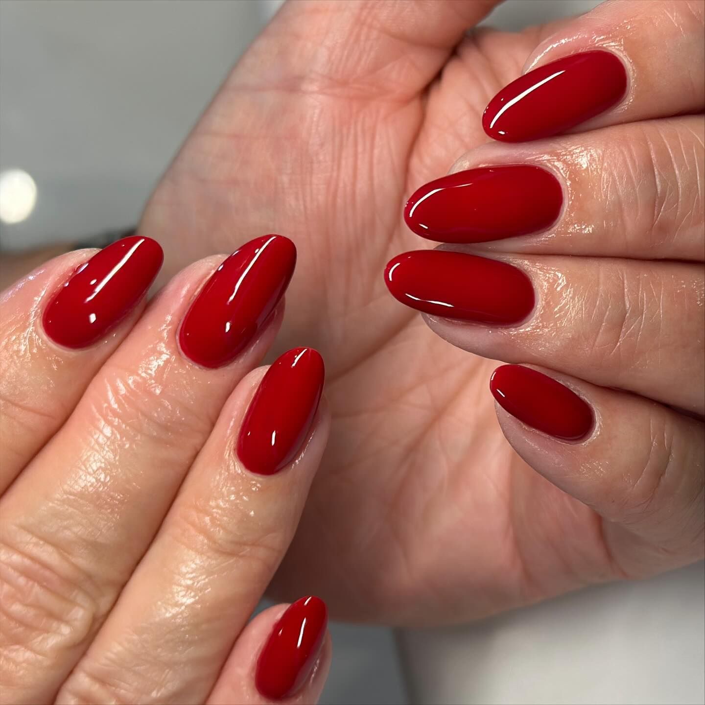 Hands with oval-shaped nails painted a glossy, vibrant red.